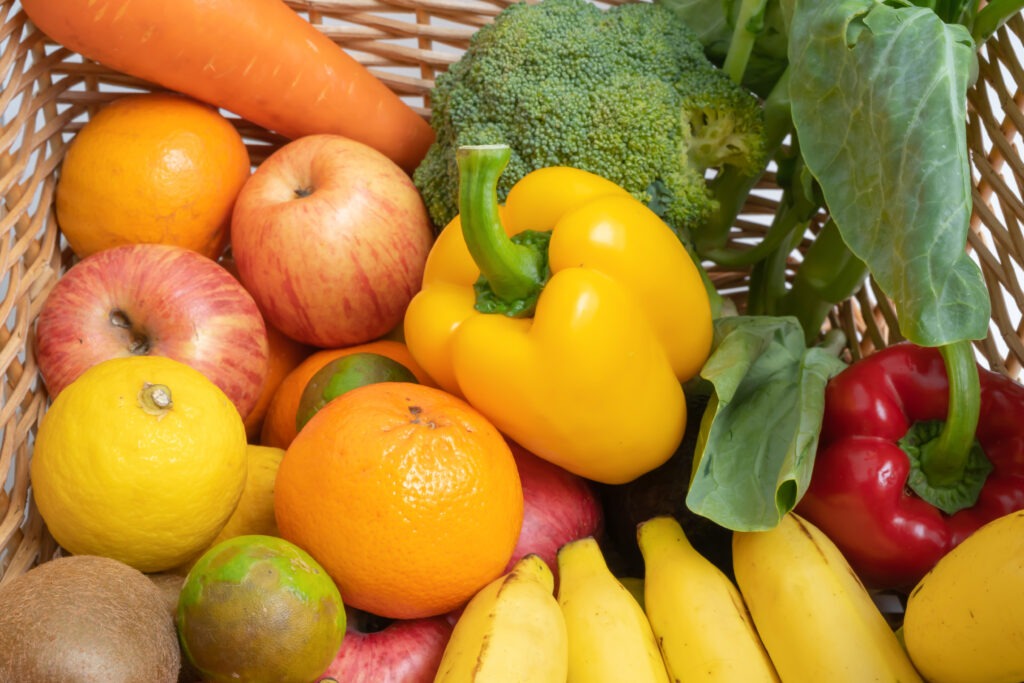 Nahaufnahme eines Weidenkorbs, prall gefüllt mit frischem, buntem Obst und Gemüse wie Äpfeln, Bananen, Orangen, Paprika, Brokkoli und Karotten. Die Vielfalt der Farben und Texturen wirkt appetitlich – ein Symbol für ausgewogene, vitaminreiche Ernährung und die Qualität der hauseigenen Frischeküche.